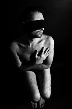 Seated handsome muscular man with a bandage over his eyes on a black background