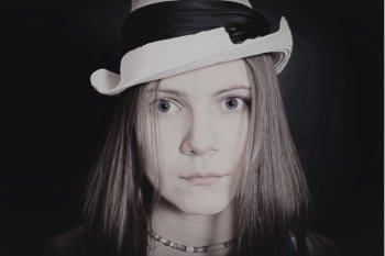 portrait of young blue-eyed girl in white hat on black background
