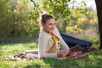 woman lying on bedding on green grass with ipad during rest in the park