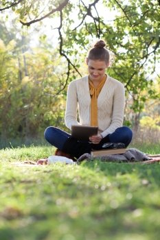 woman sitting on bedding on green grass with ipad during picknic in the park