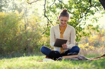 Distance education. Sitting woman using ipad during autumn fun outdoors