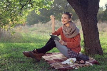 Hipster style young woman using tablet pc during a rest under the tree