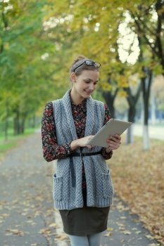 Hipster style young woman using tablet pc in autumn street
