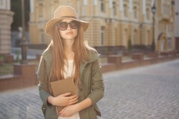 girl in hat and glasses holding book outdoors