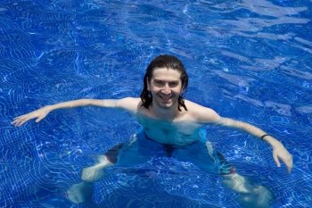Young happy man smiling on a pool with clear blue water 