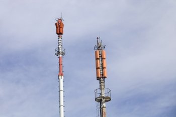 Two towers of communications with different antennas under blue sky.