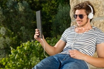casual man holding a tablet with headphones, outdoor