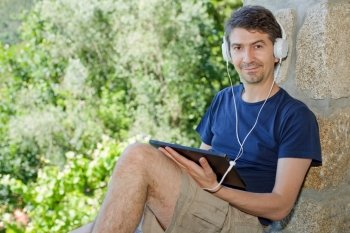 casual man holding a tablet with headphones, outdoor