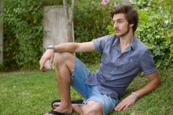 young casual man posing seated, smiling at the camera, outdoors