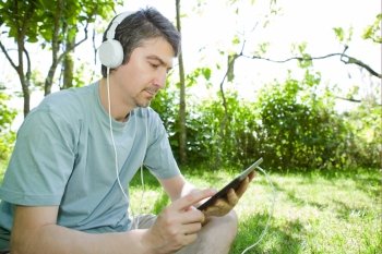 young man holding a tablet with headphones, outdoor