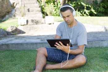 young man relaxing with a tablet pc listening music with headphones on a the park, outdoor