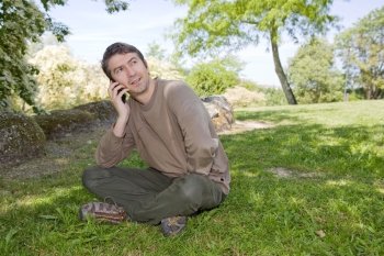 young man sitting and talk on mobile phone, against green of summer park.