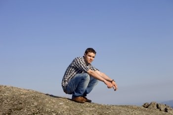 young casual man on top of a rock with the sky as background