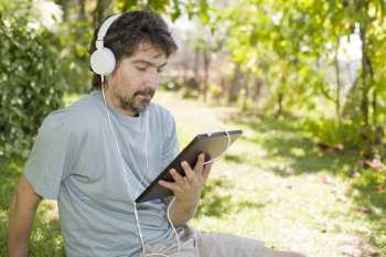 young man holding a tablet with headphones, outdoor