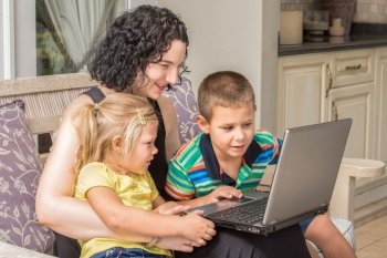 A mother and her two children, a girl and a boy, are looking with much interest at something on a silver laptop while sitting outside on the patio.