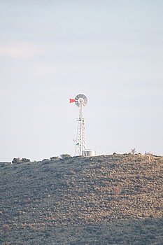 A tall wind pump stand on a hill out in the distance.