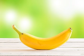 Single banana on a wooden desk on green background
