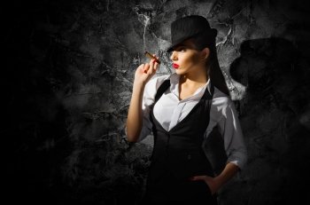 Dangerous and beautiful criminal girl with cigar on grey wall