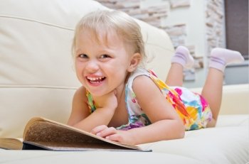 Little smiling girl with book on sofa
