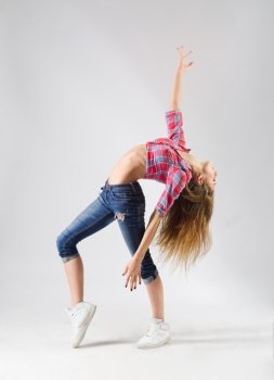 Young modern dancing girl in jeans on grey