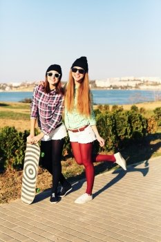 Two teen girl friends having fun together with skate board. Outdoors, urban lifestyle.
