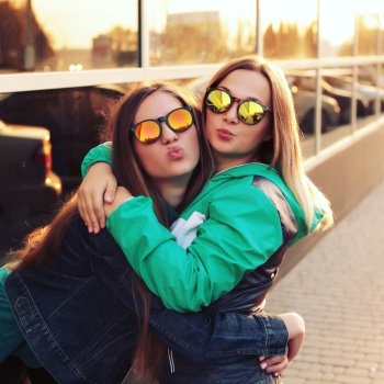 Close up fashion portrait of two young hipster girl friends, wearing mirrored sunglasses, having blonde and ombre hairs