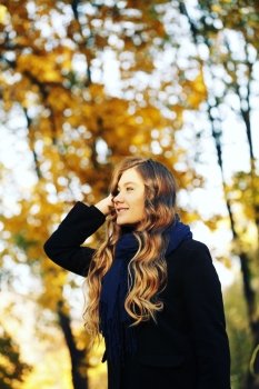 young blonde woman in autumn in park smiling wearing black coat and blue scarf