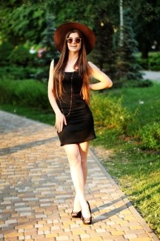 Beautiful young hipster woman outdoors, wearing black dress, hat and vintage sunglasses