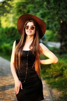 Beautiful young hipster woman outdoors, wearing black dress, hat and vintage sunglasses