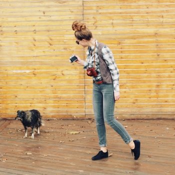 Outdoor lifestyle portrait of pretty funny hipster woman making photo. Retro photographer. Modern urban girl has fun with vintage photo camera, wooden background.