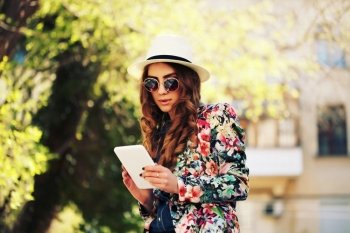 Beautiful smiling hipster woman wear vintage sunglasses, jeans shirt, white hat and jacket take a picture of herself with digital tablet. Selfie style. Toned in warm colors. Outdoors shot, lifestyle