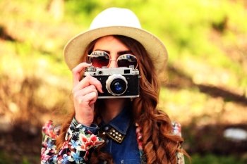 Outdoor summer lifestyle portrait of pretty young woman having fun in the city. Photographer making pictures in hipster style glasses and hat. Photo toned style Instagram filters.