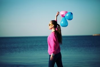 Beach woman laughing having fun in vacation holidays. Beautiful hipster girl dressed in bright youth clothes walking in the beach, holding colored balloons.