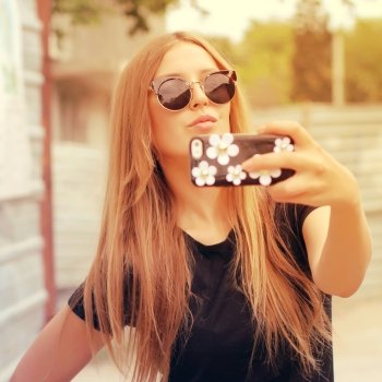 Young woman taking a selfie outdoors on sunny summer day. Photo toned style Instagram filters