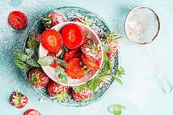Sweet sliced  Strawberries in bowls with icing sugar on light blue background, top view