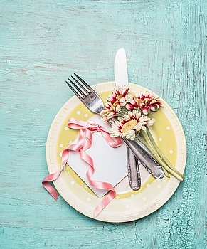 Table setting with plate, cutlery, card and pretty flowers on turquoise shabby chic background, top view
