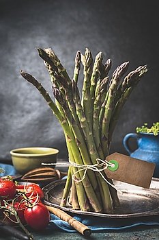 Green asparagus bunch with string and blank tag on dark rustic kitchen table with cooking ingredients