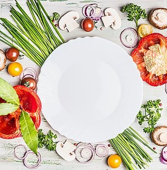 Fresh organic vegetables and seasoning ingredients for tasty vegetarian cooking around blank white plate , top view. Healthy or diet food concept.