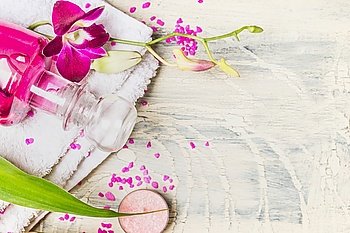 Close up of glass bottle of lotion with pink orchid flowers  on white towel on light wooden background, top view, place for text. Spa, wellness or body care concept
