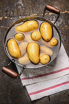 Fresh new potatoes in old pan with water on rustic wooden background , top view