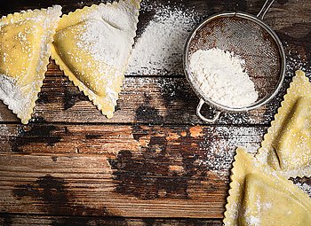 Fresh  ravioli and flour on rustic  wooden background, top view