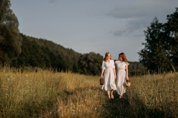 They are wearing dresses and the background shows grass, trees, and a cloudy sky. It appears to be a summery outdoor scene, possibly related to a wedding.. The image depicts two women walking in a field. 5619