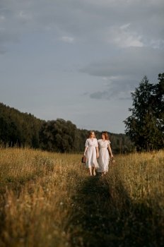 618.
It appears to be a summery outdoor scene, possibly related to a wedding.. Two women in white dresses standing in a field of tall grass with a blue sky and clouds in the background 5618.