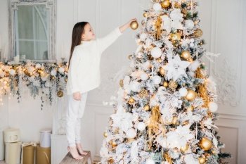 A child in a cozy sweater joyfully decorates a snow-frosted Christmas tree adorned with golden ornaments