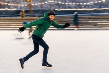 Energetic man ice skating swiftly on an urban rink with soft evening lights.
