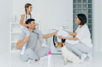 Family with a child and dog doing laundry together in a white, organized laundry room