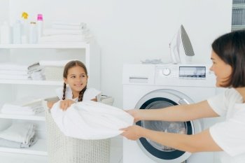Mother and daughter enjoying laundry time together in a white, sunny room.