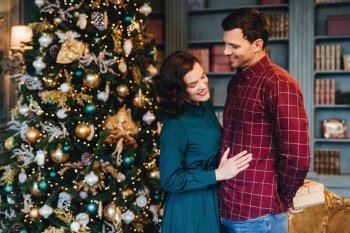 Loving couple in festive attire embracing in front of a beautifully decorated Christmas tree, sharing a tender moment