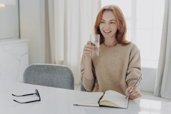 Smiling redhead woman with a glass of water and notebook, taking a healthy break