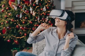 Delighted woman experiencing virtual reality with a VR headset, Christmas tree backdrop